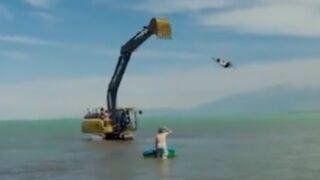 Excavator swings a man around in circles then suddenly stops smashing him into the arm of the Excavator